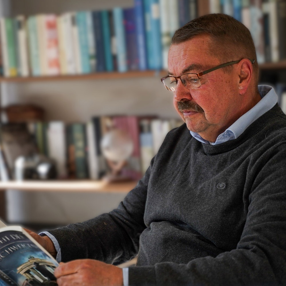 Ein Buch schreiben & Autor werden Ein Buch schreiben Reiner mit Buch auf Stuhl